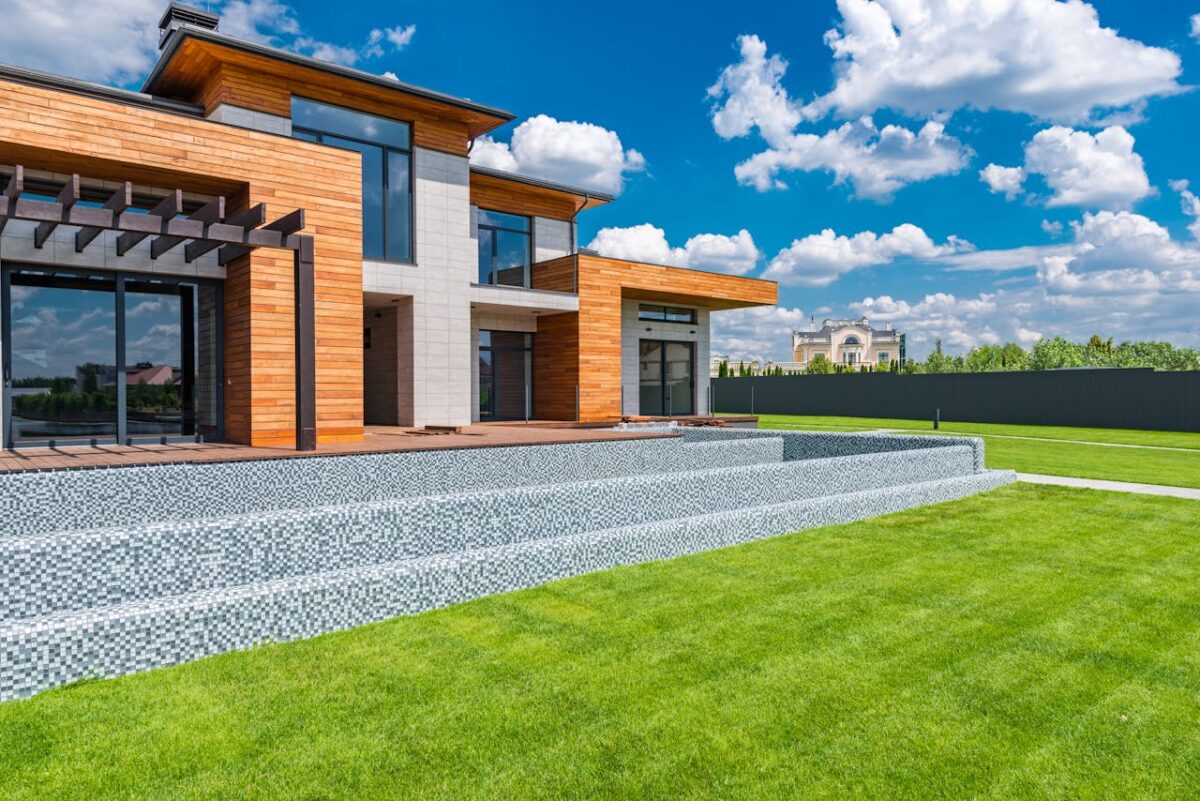 services-01 Exterior of contemporary residential house with panoramic windows glass doors and green lawn in yard on sunny day against blue sky with white clouds