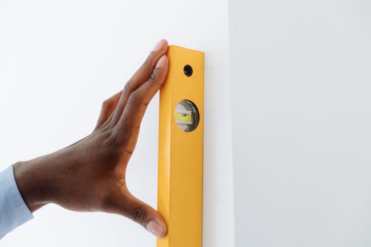 get-in-touch A close-up of a hand using a yellow level tool against a white wall to ensure vertical alignment.