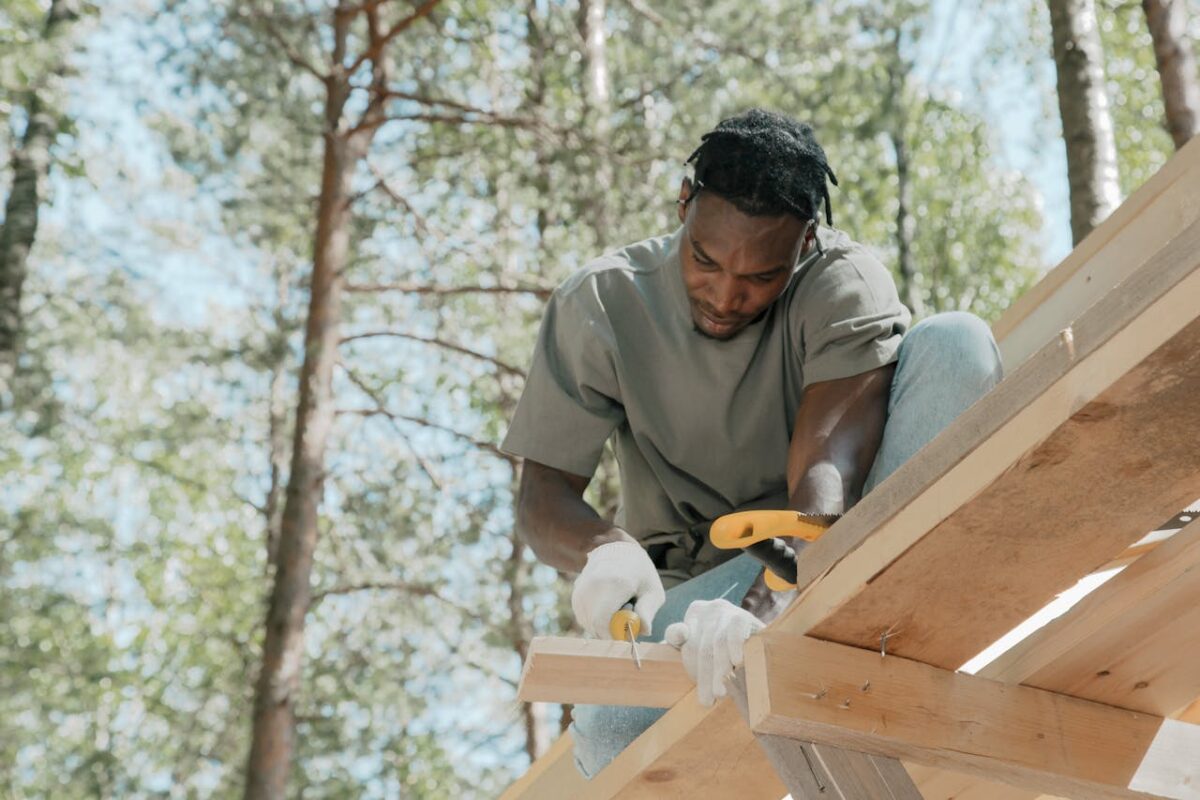 Skilled carpenter focused on building a wooden structure outdoors on a sunny day.